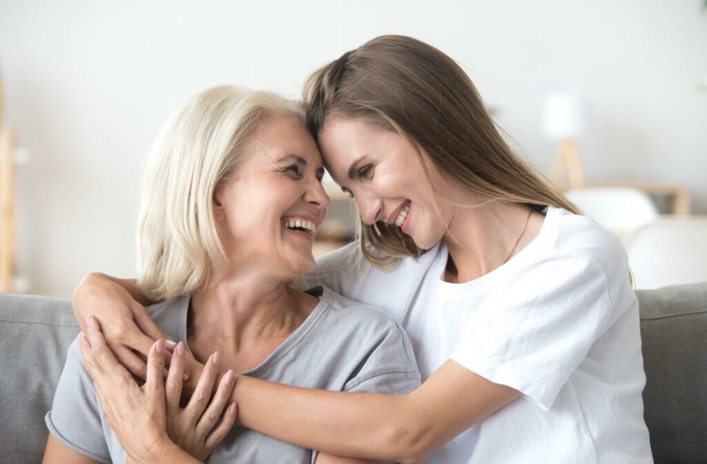 An older woman and young adult daughter hugging and smiling at each other.