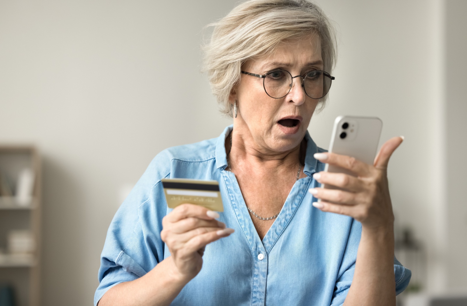 Shocked mature woman holding credit card staring at cell phone.