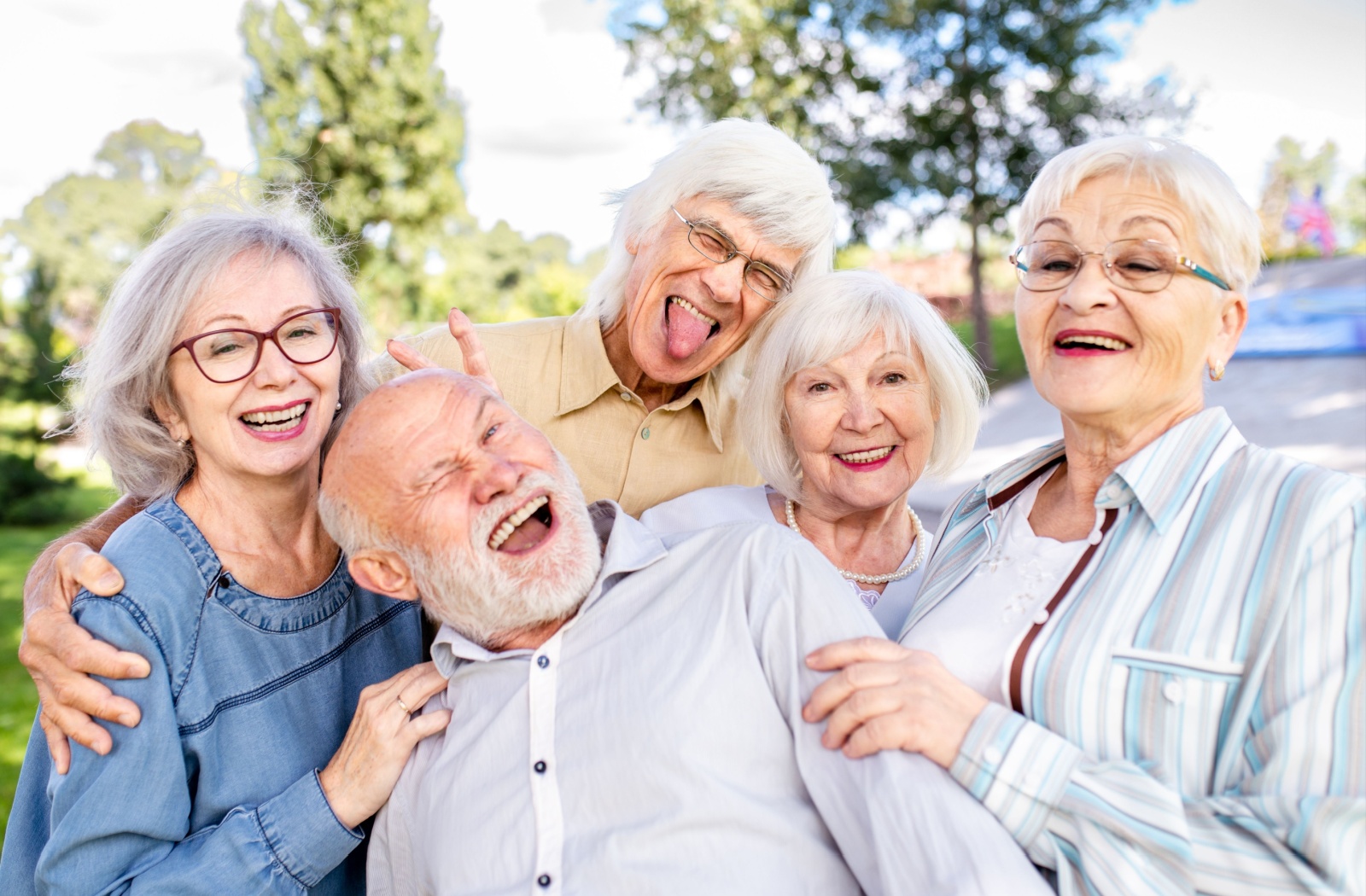 A group of five seniors pose together outdoors while making goofy faces or laughing while their picture is taken