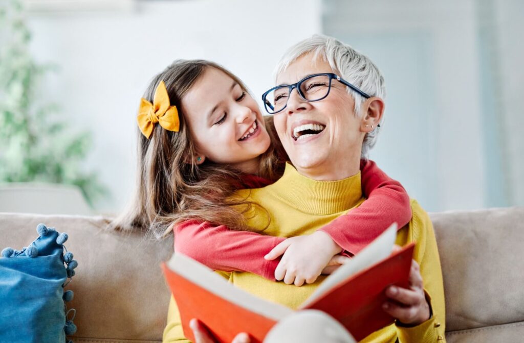 A happy senior reads a story with their young grandchild who was able to visit because of their proximity to the assisted living community.