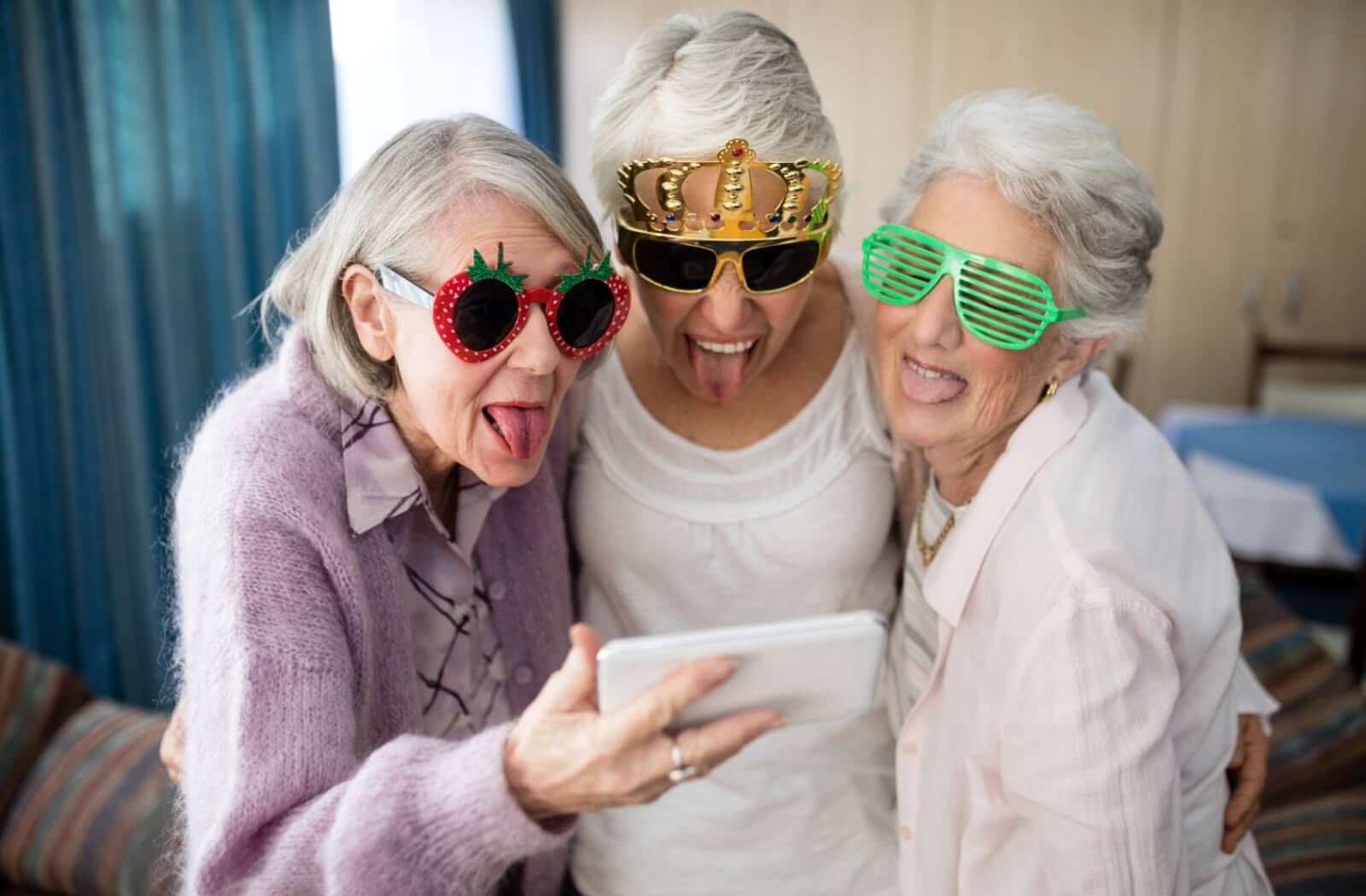 A smiling group of seniors taking funny selfies together to send to their loved ones.