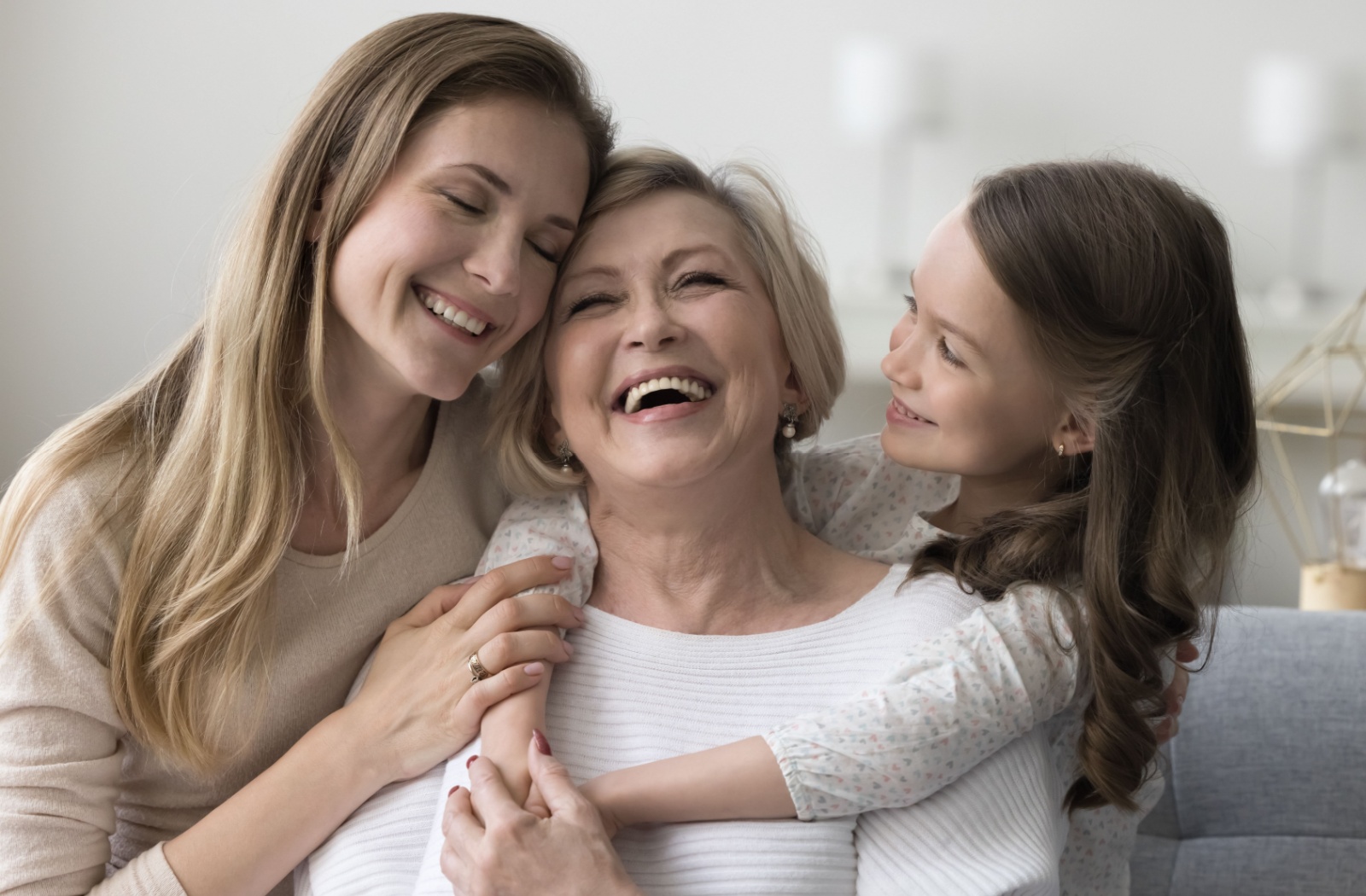 An adult child and her daughter laughing and visiting with her mother in an assisted living community.