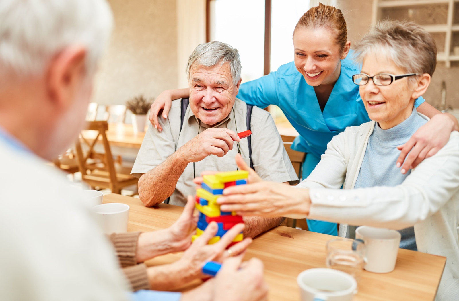 A young senior living staff member engages with a group of older adults playing jenga together.