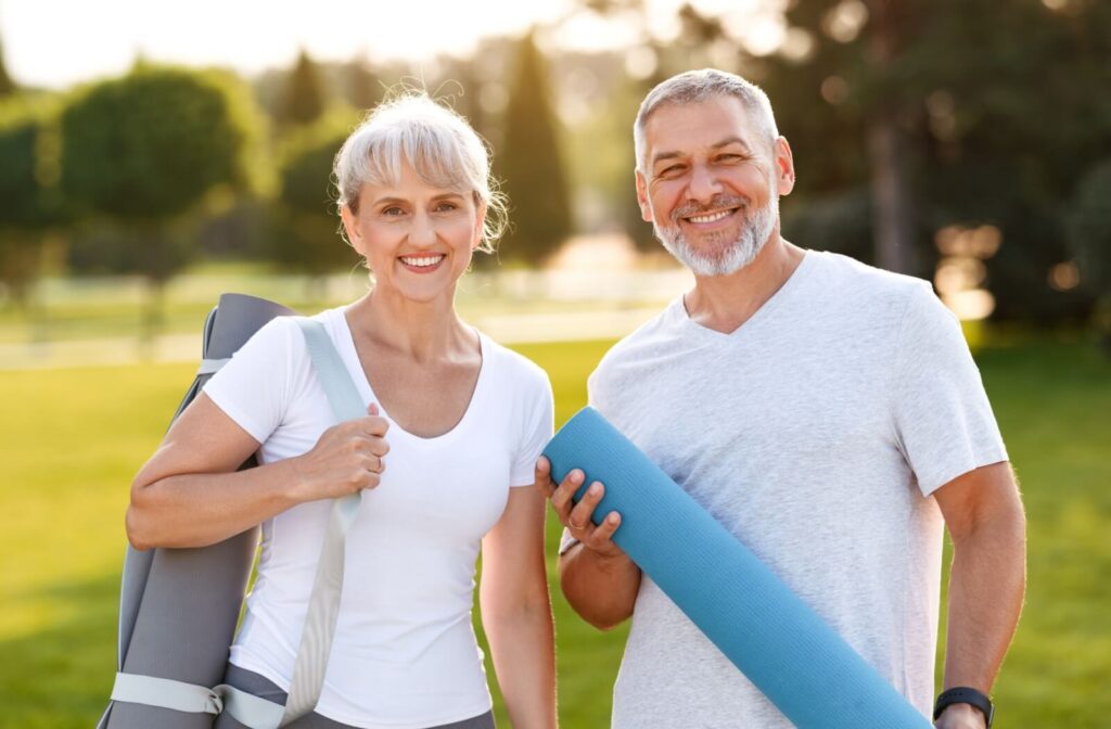 Two older adults with yoga mats get ready for a yoga class in the park offered by their senior living community.