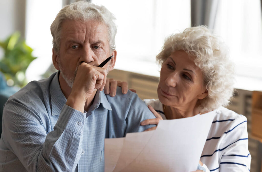 An older adult comforts their spouse in their home while they check notes on a memory test together