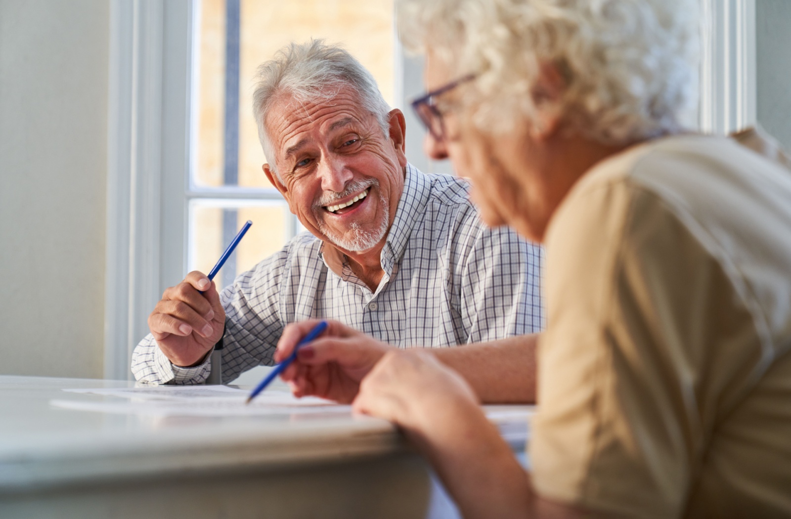 Two older adults laugh with each other while using pens to take a memory test together