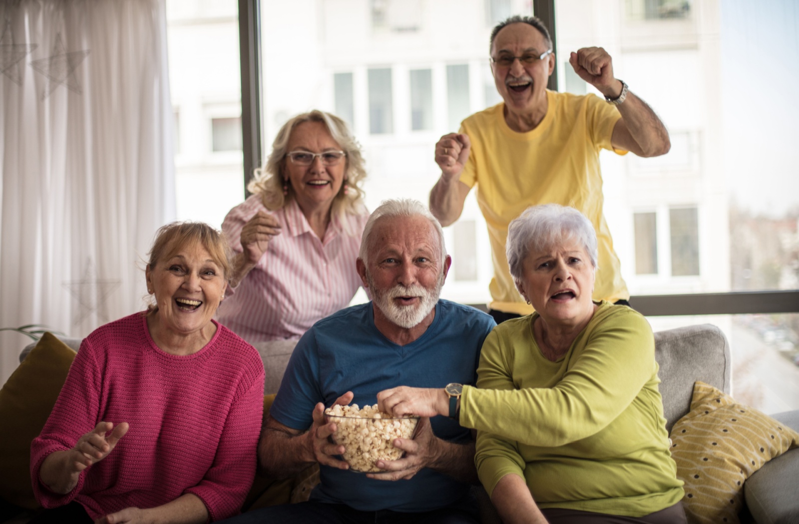 Five seniors gather on a couch with popcorn to watch the unfolding of their favorite TV program together