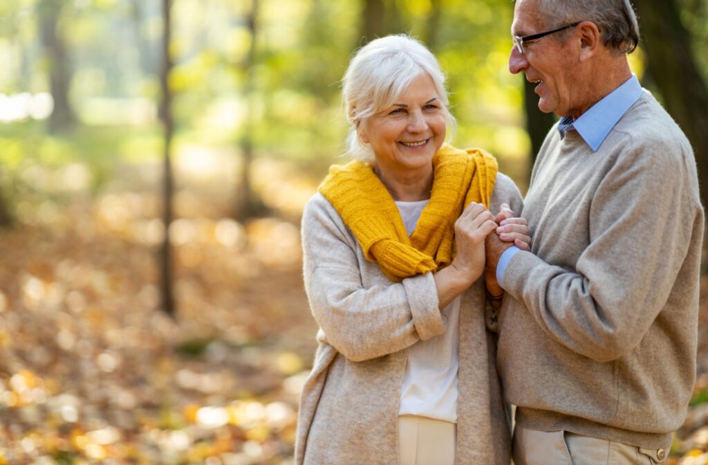 Older adults smiling and holding hands while walking together in a park surrounded by colorful fall leaves