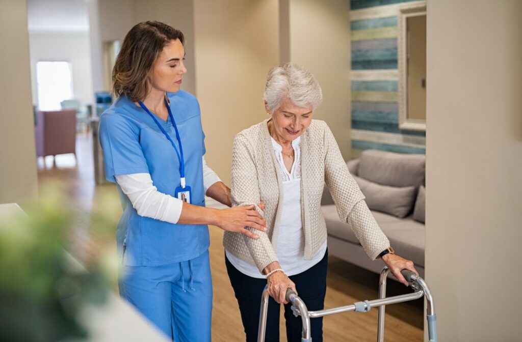 A female nurse helping an elderly woman with a walker walk across the nursing home lobby.